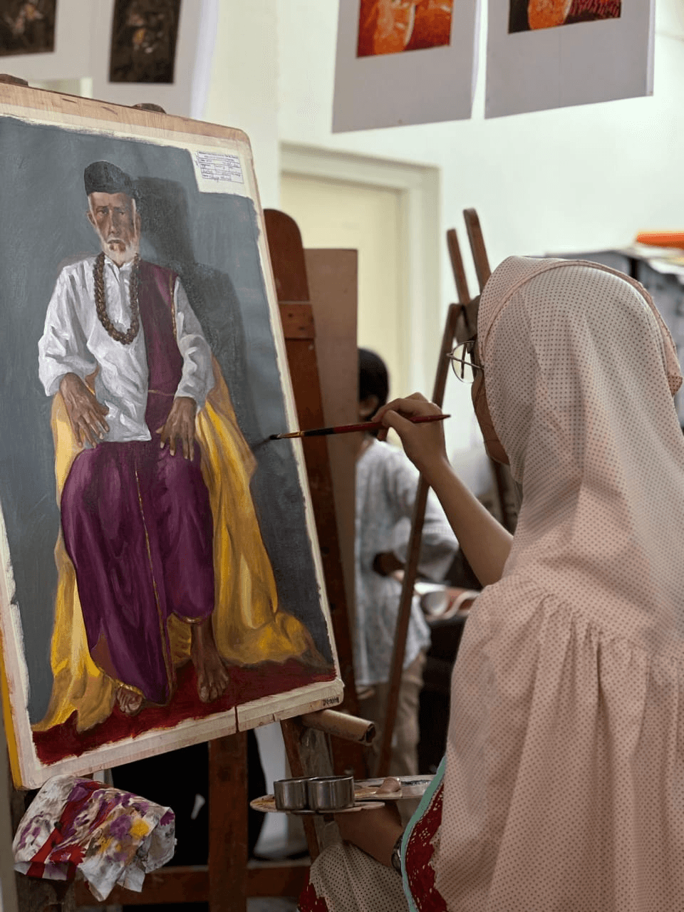 Naqiya Attarwala painting a full-length portrait on an easel in her studio, brush in hand